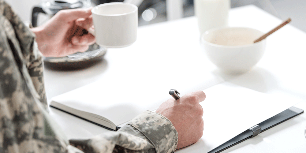 Military man sitting at the table with a notebook and coffee.